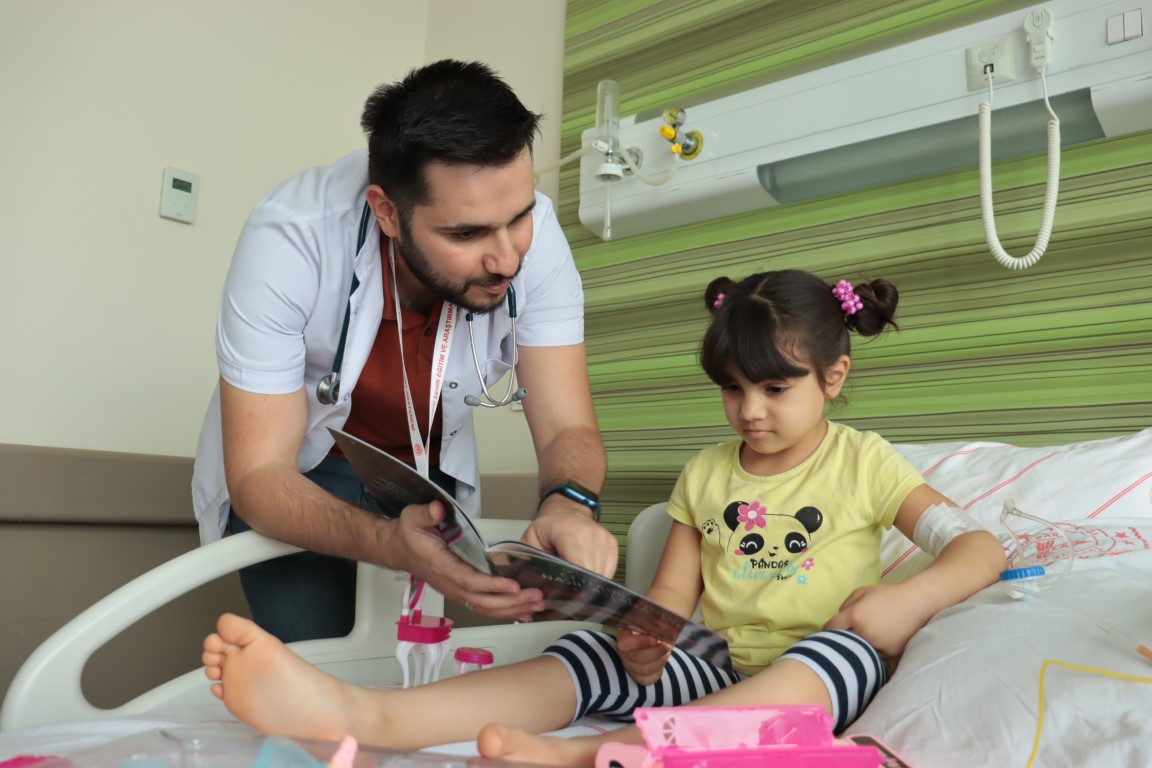 Çocuk doktoru yazdığı hikaye kitabını servis servis gezerek çocuklara okuyor