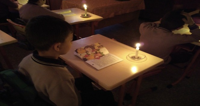 Minik öğrenciler mum ışığı eşliğinde kitap okuyor