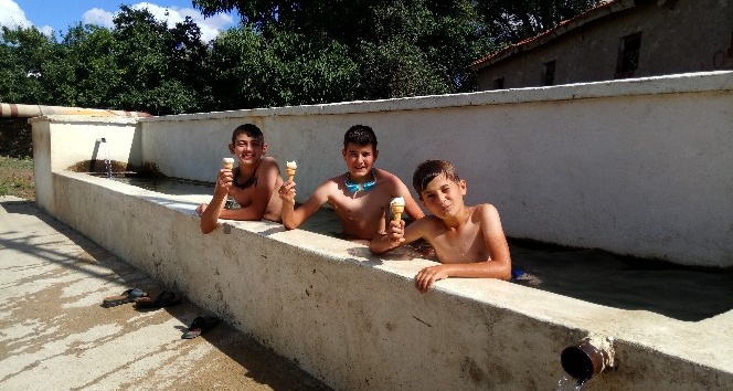 Sıcaklardan bunalan çocuklar köy meydanındaki su oluğunda serinliyor